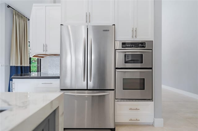 kitchen featuring white cabinets, appliances with stainless steel finishes, light stone countertops, and tasteful backsplash