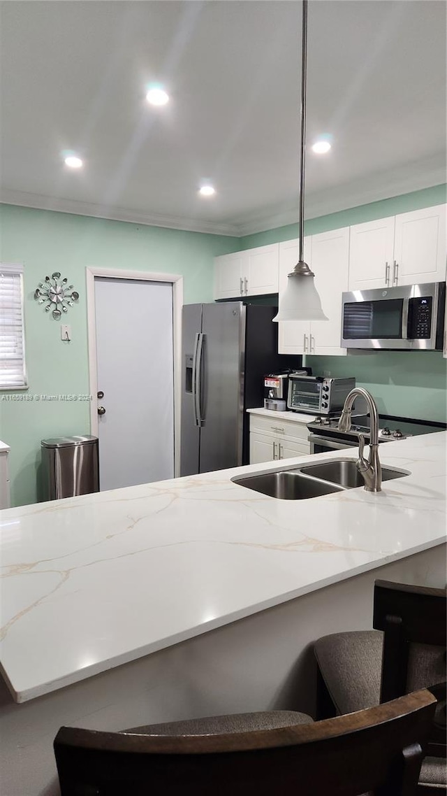 kitchen with light stone countertops, pendant lighting, stainless steel appliances, and white cabinets