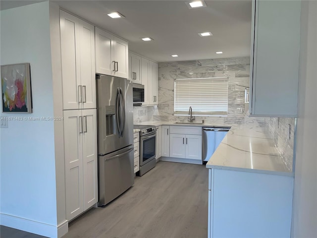 kitchen with light stone counters, sink, white cabinetry, light hardwood / wood-style flooring, and appliances with stainless steel finishes