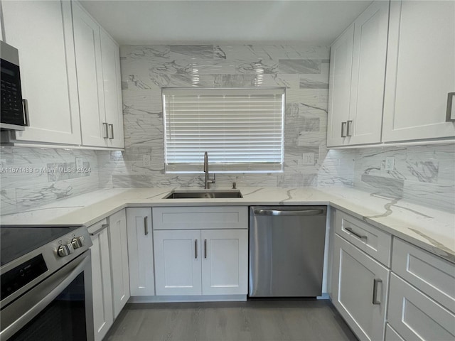 kitchen with light stone counters, sink, white cabinetry, appliances with stainless steel finishes, and hardwood / wood-style floors