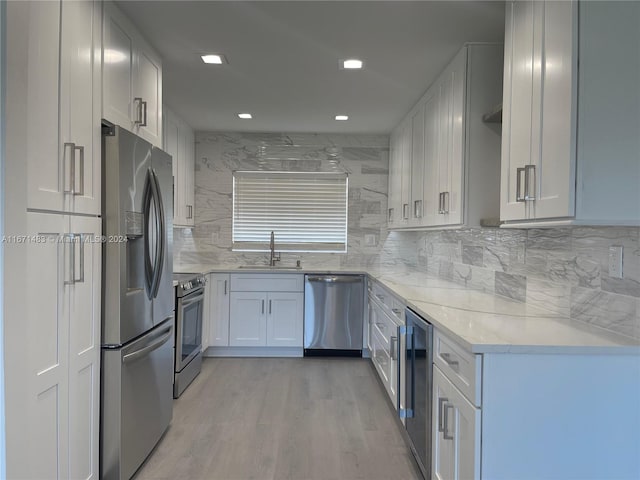 kitchen with decorative backsplash, stainless steel appliances, white cabinets, and light hardwood / wood-style floors