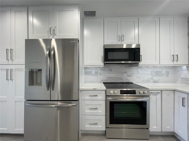 kitchen featuring light stone countertops, stainless steel appliances, backsplash, and white cabinetry