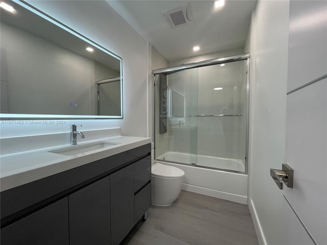 full bathroom featuring wood-type flooring, bath / shower combo with glass door, vanity, and toilet