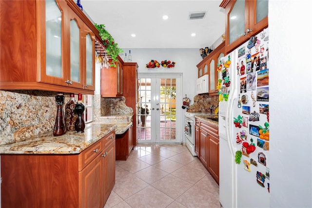 kitchen with light tile patterned flooring, tasteful backsplash, white appliances, french doors, and light stone countertops