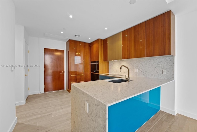 kitchen with kitchen peninsula, decorative backsplash, sink, and black double oven