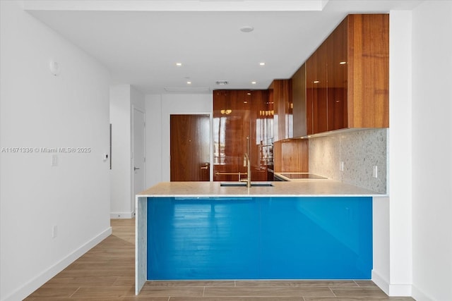 kitchen with backsplash, kitchen peninsula, sink, and light wood-type flooring