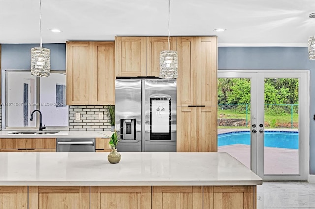 kitchen featuring light brown cabinetry, sink, hanging light fixtures, stainless steel appliances, and decorative backsplash