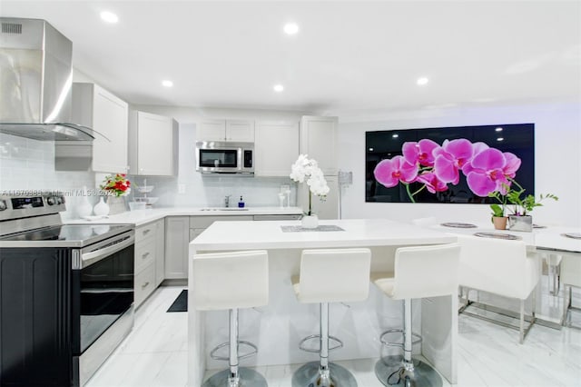 kitchen with appliances with stainless steel finishes, decorative backsplash, wall chimney exhaust hood, a breakfast bar area, and sink