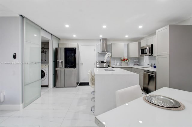 kitchen featuring washer / dryer, a center island, tasteful backsplash, wall chimney range hood, and appliances with stainless steel finishes