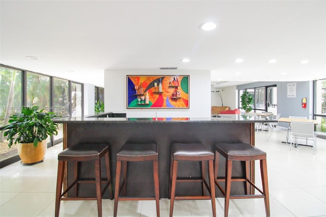 kitchen featuring a kitchen breakfast bar, a wall of windows, light tile patterned flooring, and plenty of natural light