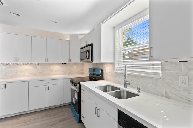 kitchen with sink, tasteful backsplash, white cabinetry, black appliances, and light hardwood / wood-style floors