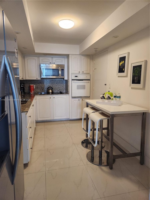 kitchen with stainless steel appliances, white cabinets, tasteful backsplash, and a breakfast bar area