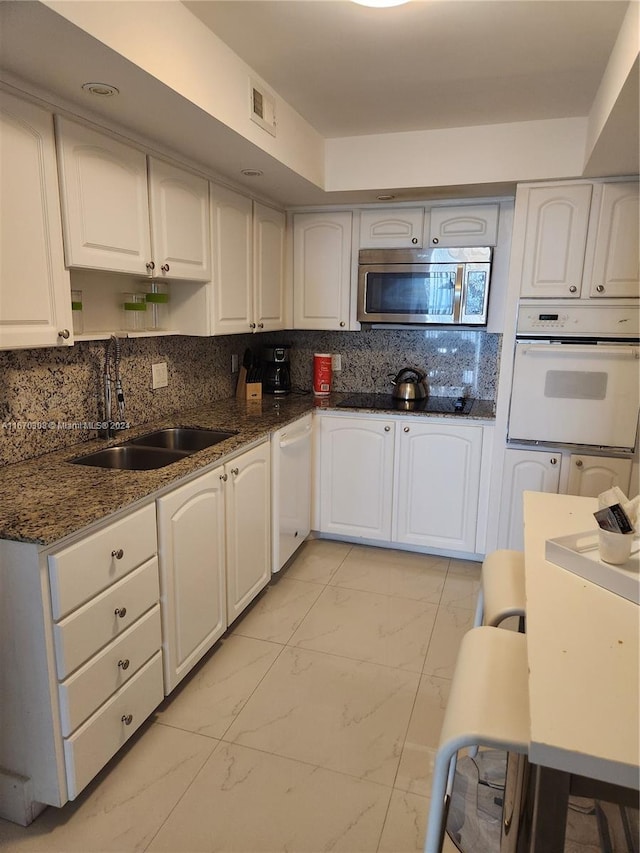 kitchen with white appliances, dark stone counters, sink, decorative backsplash, and white cabinetry