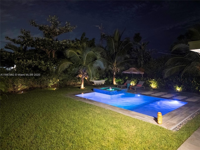 pool at night featuring an in ground hot tub and a lawn