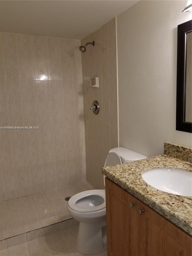 bathroom featuring vanity, tile patterned flooring, toilet, and tiled shower