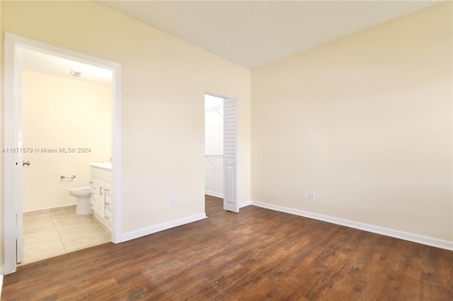 unfurnished bedroom with ensuite bath, a closet, a walk in closet, and dark hardwood / wood-style flooring