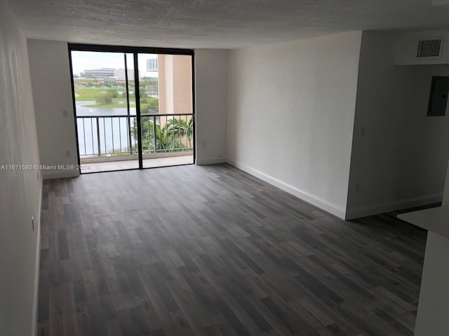 unfurnished room with a textured ceiling, a wall of windows, dark wood-type flooring, and a water view