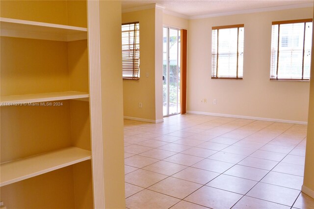 unfurnished room with tile patterned flooring, ornamental molding, and baseboards