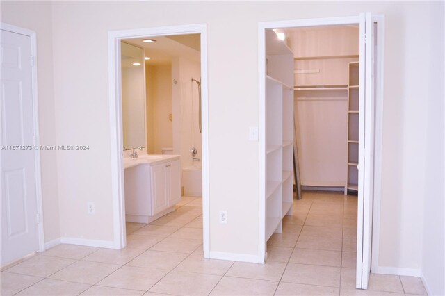 unfurnished bedroom with light tile patterned flooring, a sink, a walk in closet, baseboards, and a closet