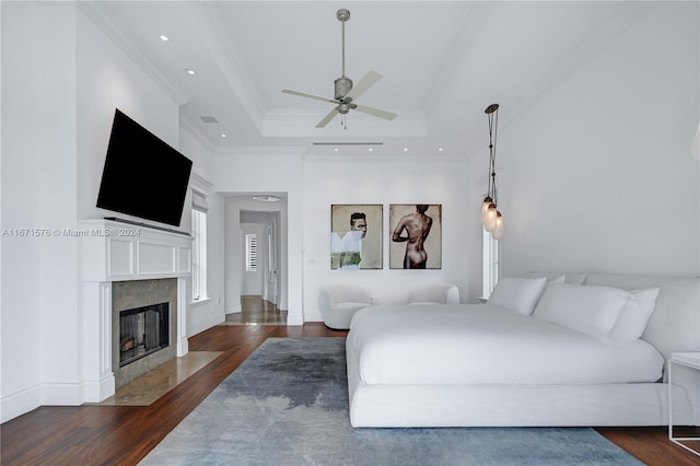 bedroom featuring dark hardwood / wood-style flooring, a high end fireplace, a tray ceiling, ceiling fan, and ornamental molding