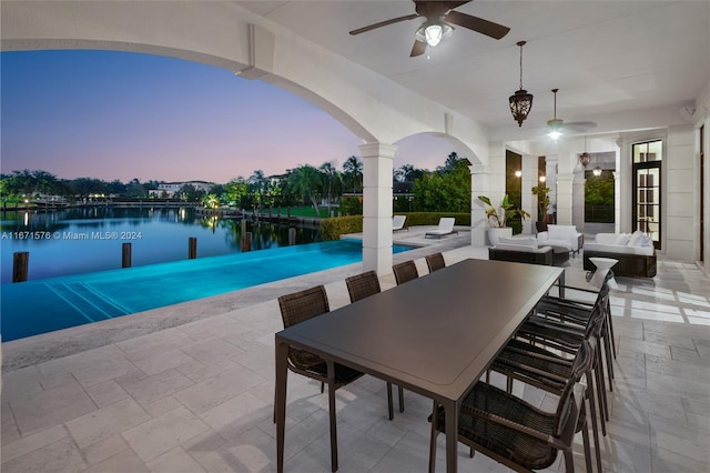 pool at dusk featuring a water view, an outdoor living space, ceiling fan, and a patio area