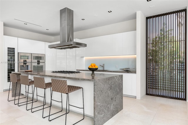 kitchen with white cabinets, a kitchen island, island range hood, and dark stone countertops