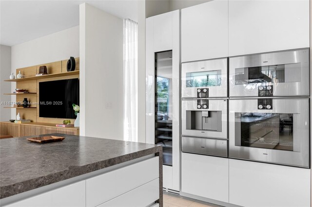 kitchen with light stone countertops, decorative light fixtures, a spacious island, white cabinets, and island exhaust hood