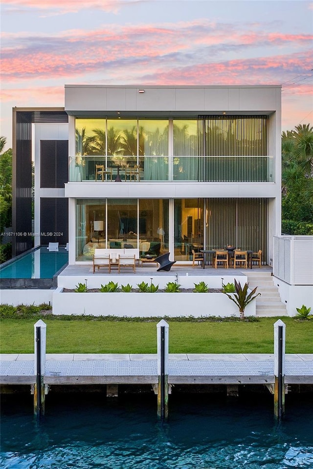 back house at dusk with a patio, a lawn, and a water view