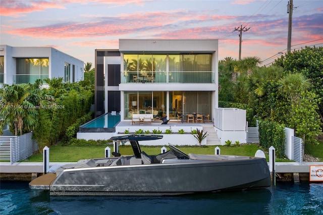 back house at dusk featuring a swimming pool, a sunroom, a patio, and a water view