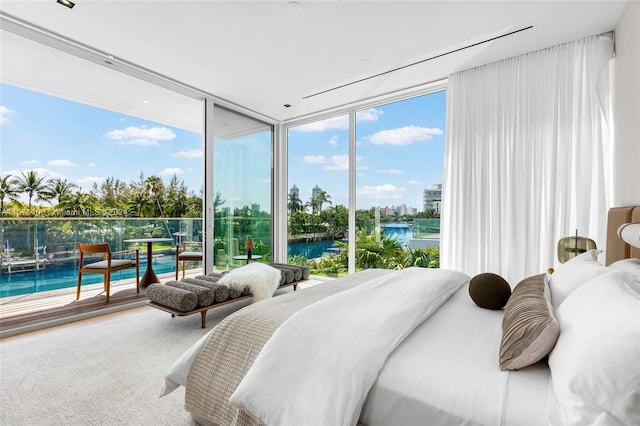 bedroom with expansive windows, a water view, and access to exterior