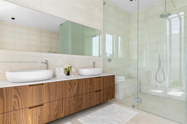 bathroom with a shower with door, vanity, tile patterned floors, and tile walls