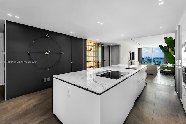 kitchen with black electric stovetop, white cabinetry, a spacious island, and sink