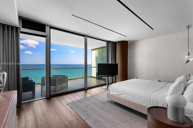 bedroom featuring light wood-type flooring, access to outside, a water view, and expansive windows