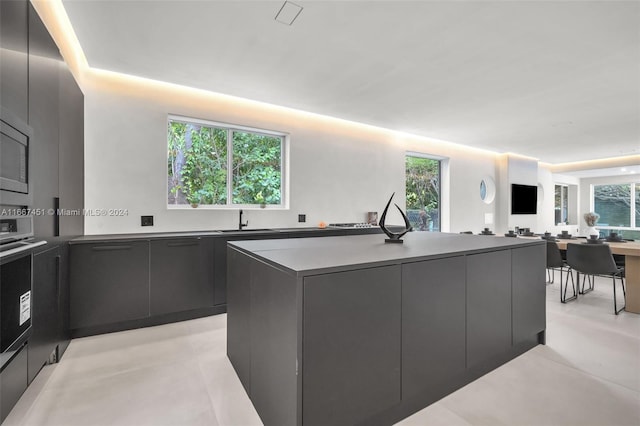 kitchen with black oven, a kitchen island with sink, plenty of natural light, and sink