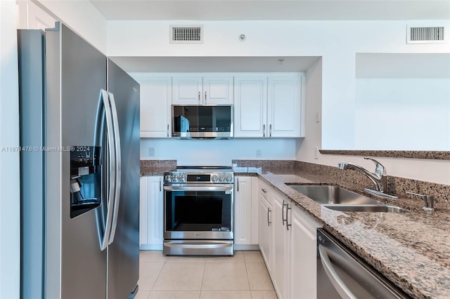 kitchen featuring sink, light tile patterned flooring, dark stone counters, white cabinets, and appliances with stainless steel finishes