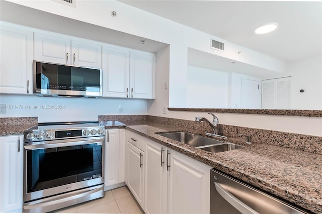 kitchen with dark stone counters, stainless steel appliances, sink, light tile patterned floors, and white cabinetry