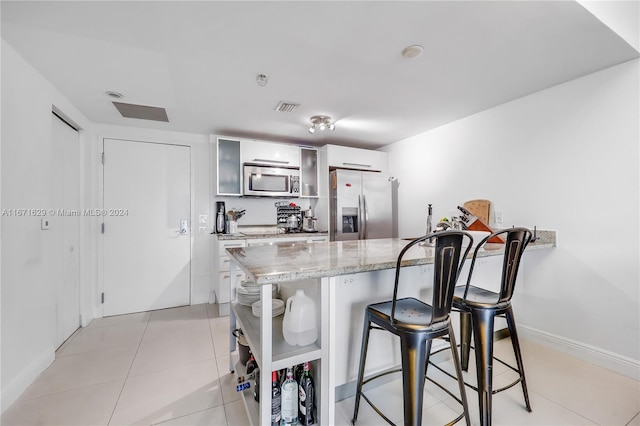 kitchen with stainless steel appliances, a kitchen bar, light tile patterned floors, white cabinets, and light stone counters