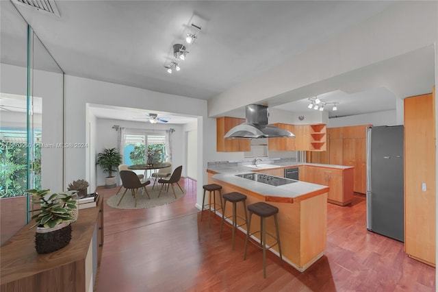 kitchen featuring a breakfast bar, black appliances, light hardwood / wood-style floors, kitchen peninsula, and island exhaust hood