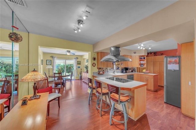 kitchen featuring kitchen peninsula, stainless steel fridge, light hardwood / wood-style flooring, and island exhaust hood