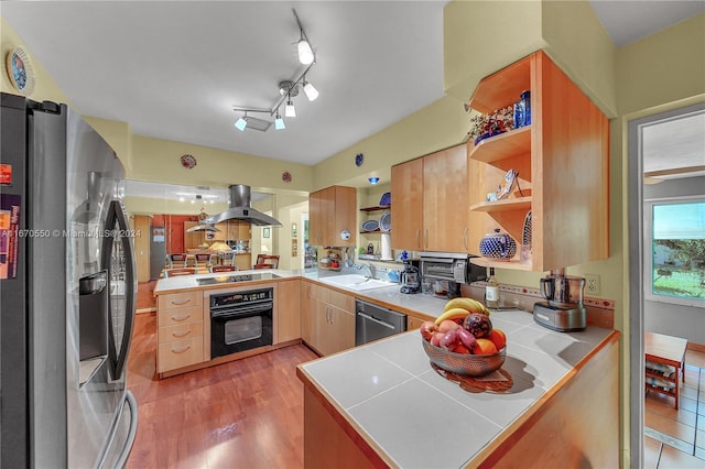 kitchen featuring tile countertops, black appliances, sink, kitchen peninsula, and island exhaust hood