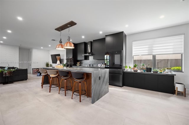 kitchen with a large island, tasteful backsplash, hanging light fixtures, black refrigerator, and wall chimney exhaust hood