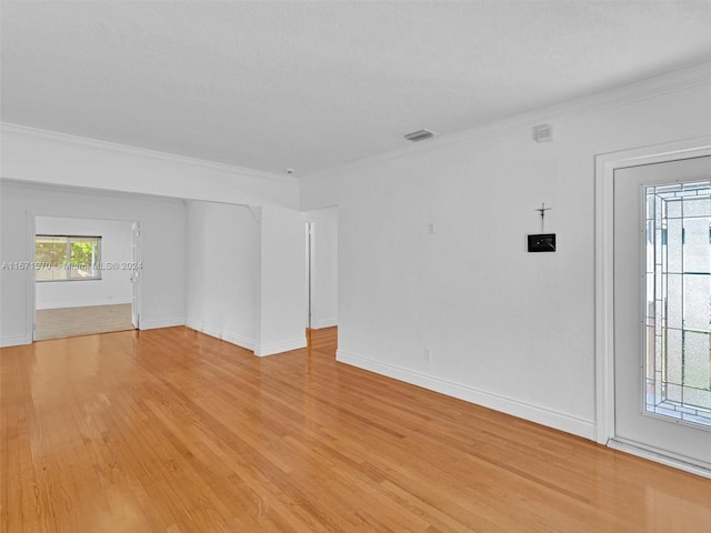 empty room with light wood-type flooring, crown molding, and a textured ceiling