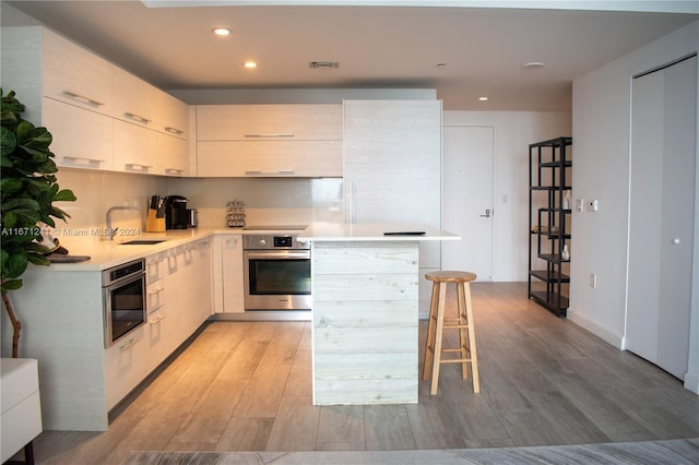 kitchen featuring light wood-type flooring, oven, a breakfast bar area, and sink