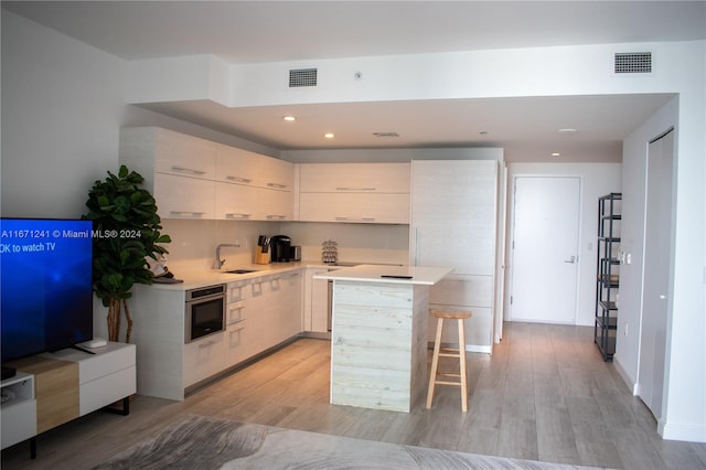 kitchen featuring a kitchen breakfast bar, light wood-type flooring, oven, and sink