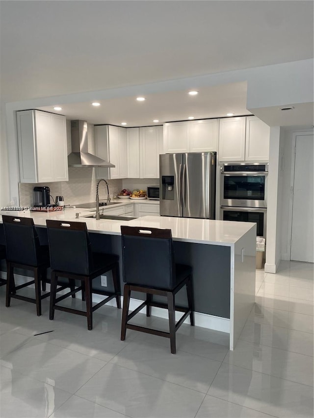 kitchen featuring light countertops, decorative backsplash, appliances with stainless steel finishes, a kitchen breakfast bar, and wall chimney exhaust hood