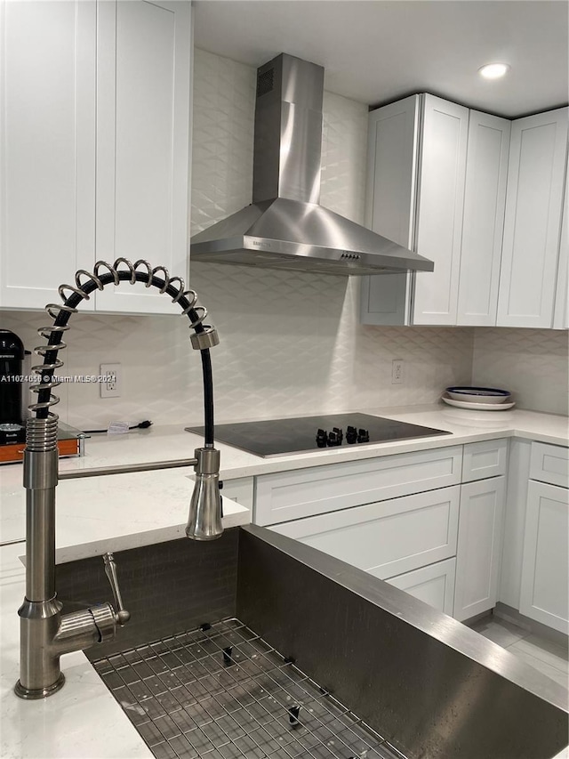 kitchen featuring black electric cooktop, white cabinets, backsplash, and wall chimney range hood