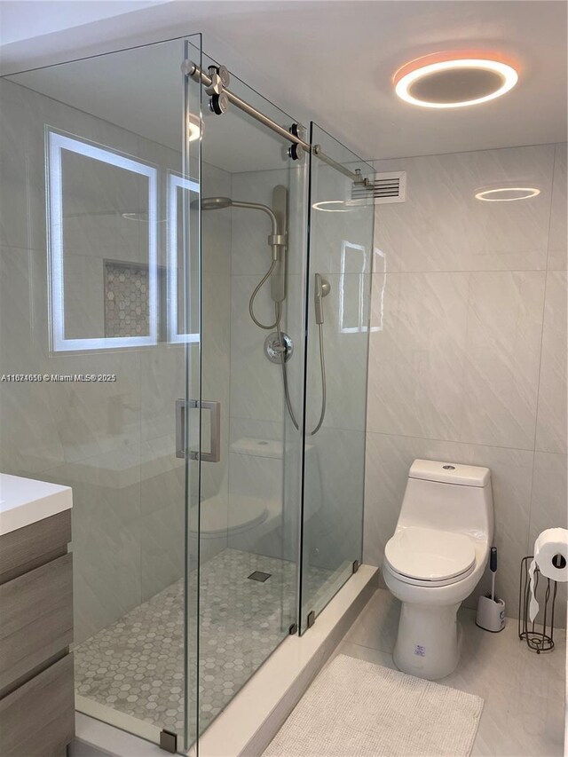 bathroom featuring vanity, tile walls, tile patterned flooring, a shower with shower door, and toilet