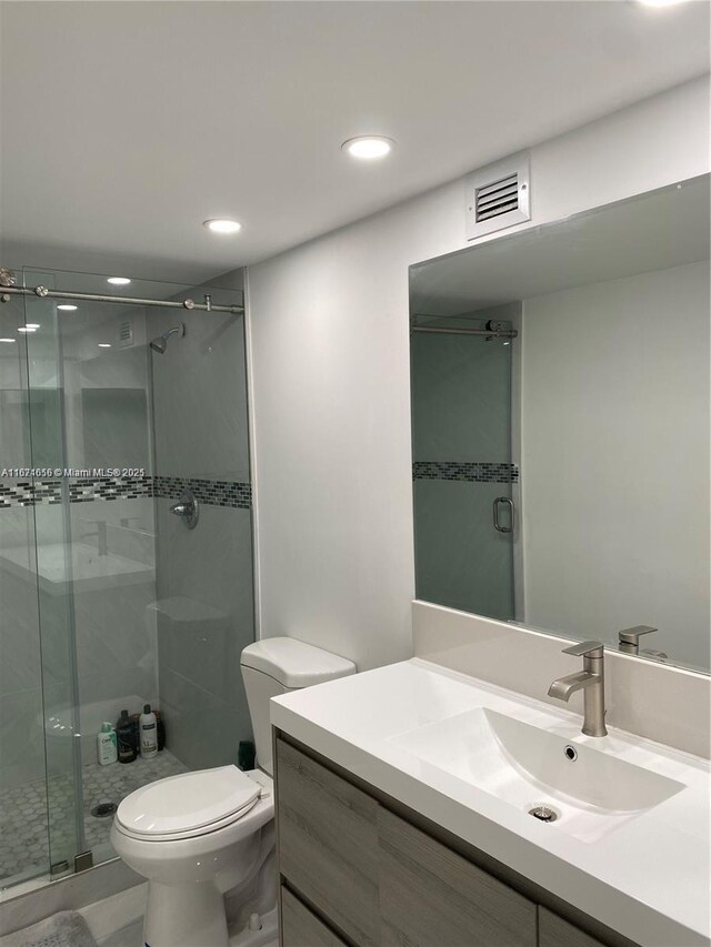 bathroom featuring a shower with shower door, vanity, and toilet