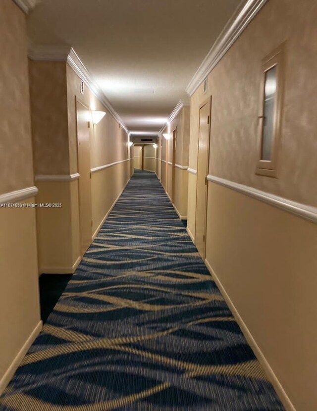 hallway with ornamental molding and dark colored carpet