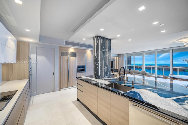 kitchen with light brown cabinets, sink, stainless steel appliances, dark stone counters, and a water view